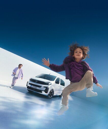Ein Kind springt und hat Spaß vor einem stehenden weißen Opel Minivan