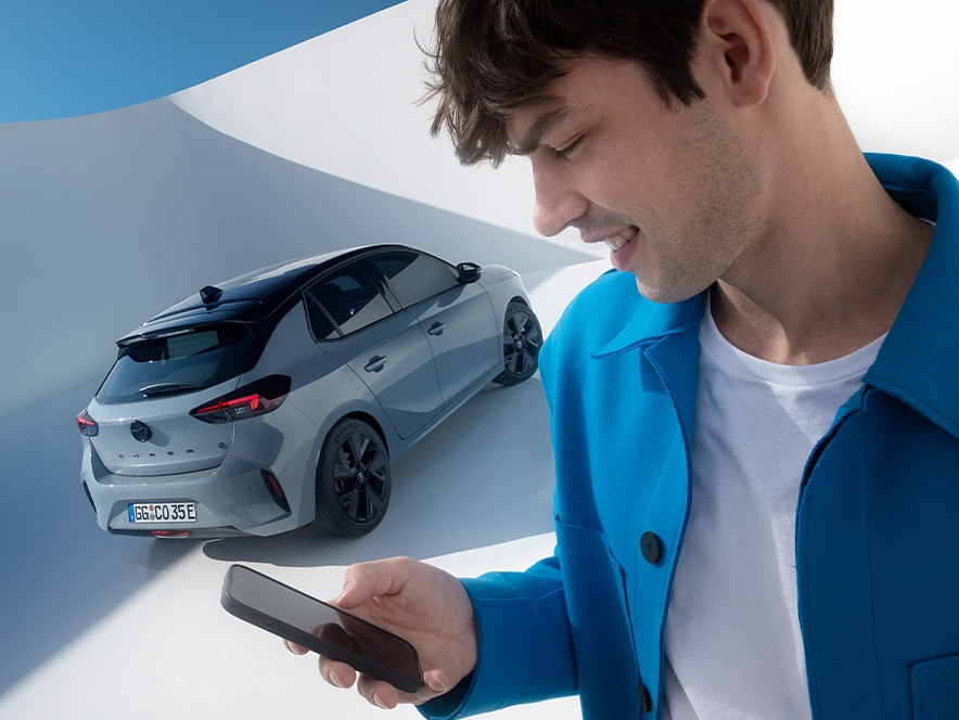Man holding phone using OpelConnect and MyOpel app with grey Opel Corsa Electric with black alloys in the background
