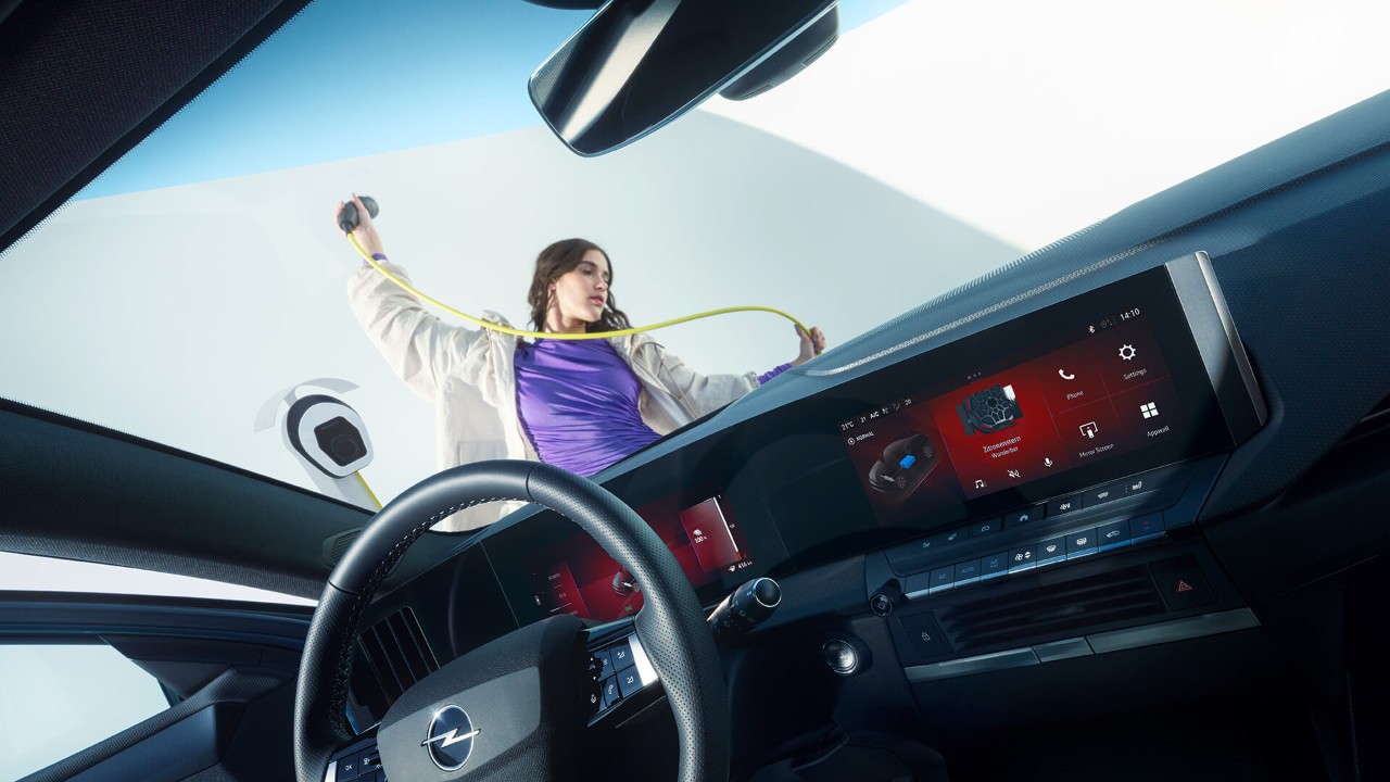 Nahaufnahme des Innenraums eines Opel Astra Sports Tourer Electric mit einer Frau, die ein Ladekabel in der Hand hält