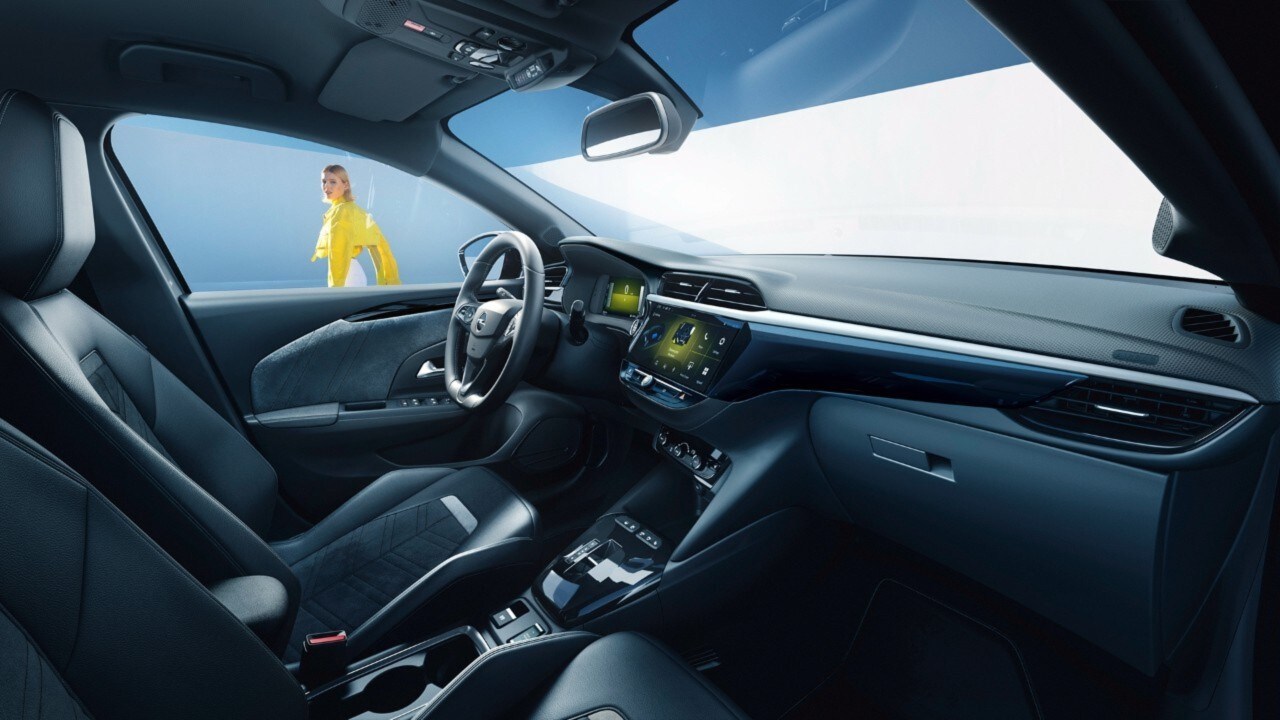 Opel Corsa Electric schwarzer Innenraum Seitenansicht vom Beifahrersitz mit Frau im Hintergrund in gelbem Hemd