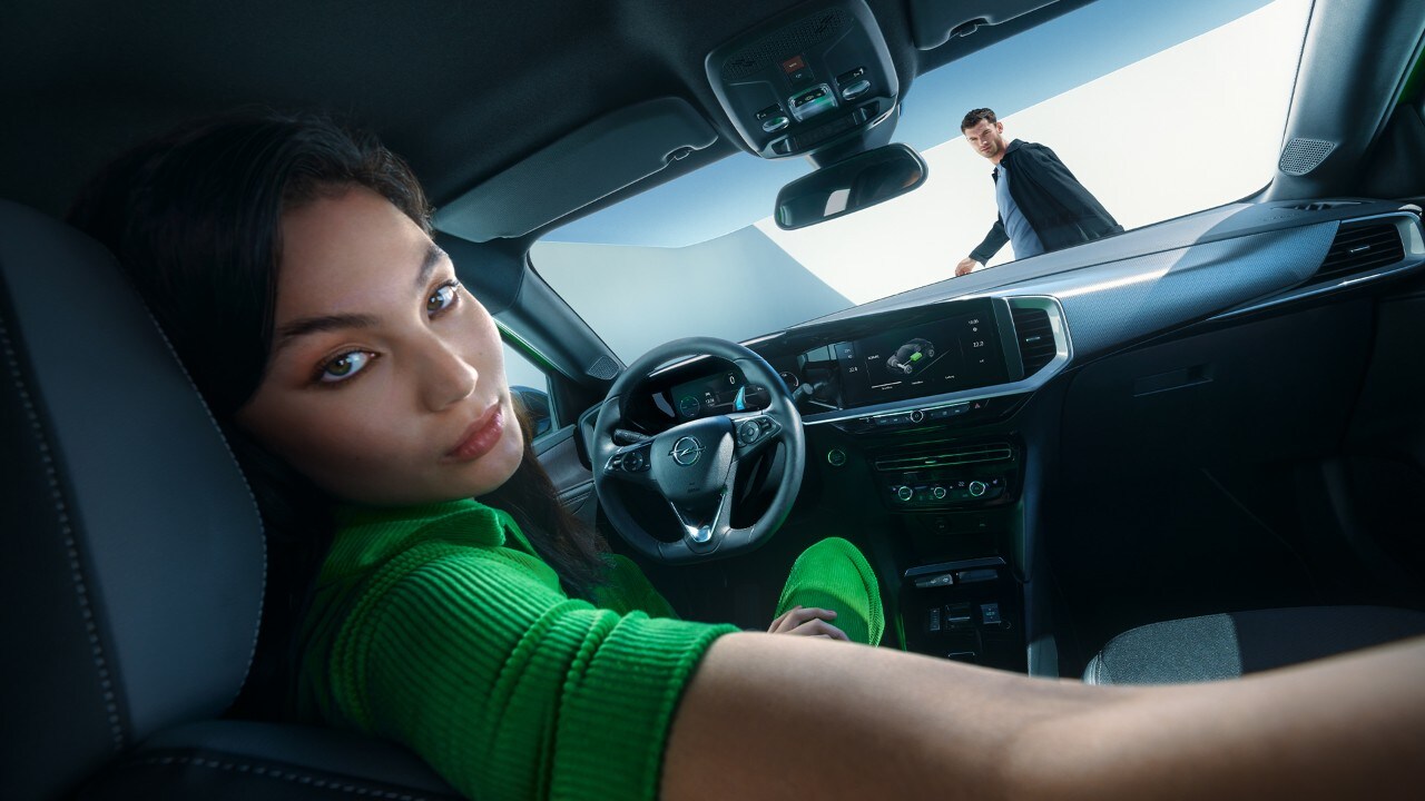 Eine Frau blickt auf dem Fahrersitz eines Opel Mokka Electric nach hinten, während draußen ein Mann geht